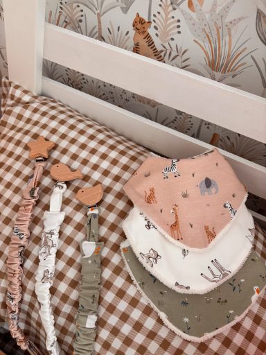 Conjunto de chupeteros para bebé Baberos de tela con diseños de animales sobre una superficie de cuadro marrón.